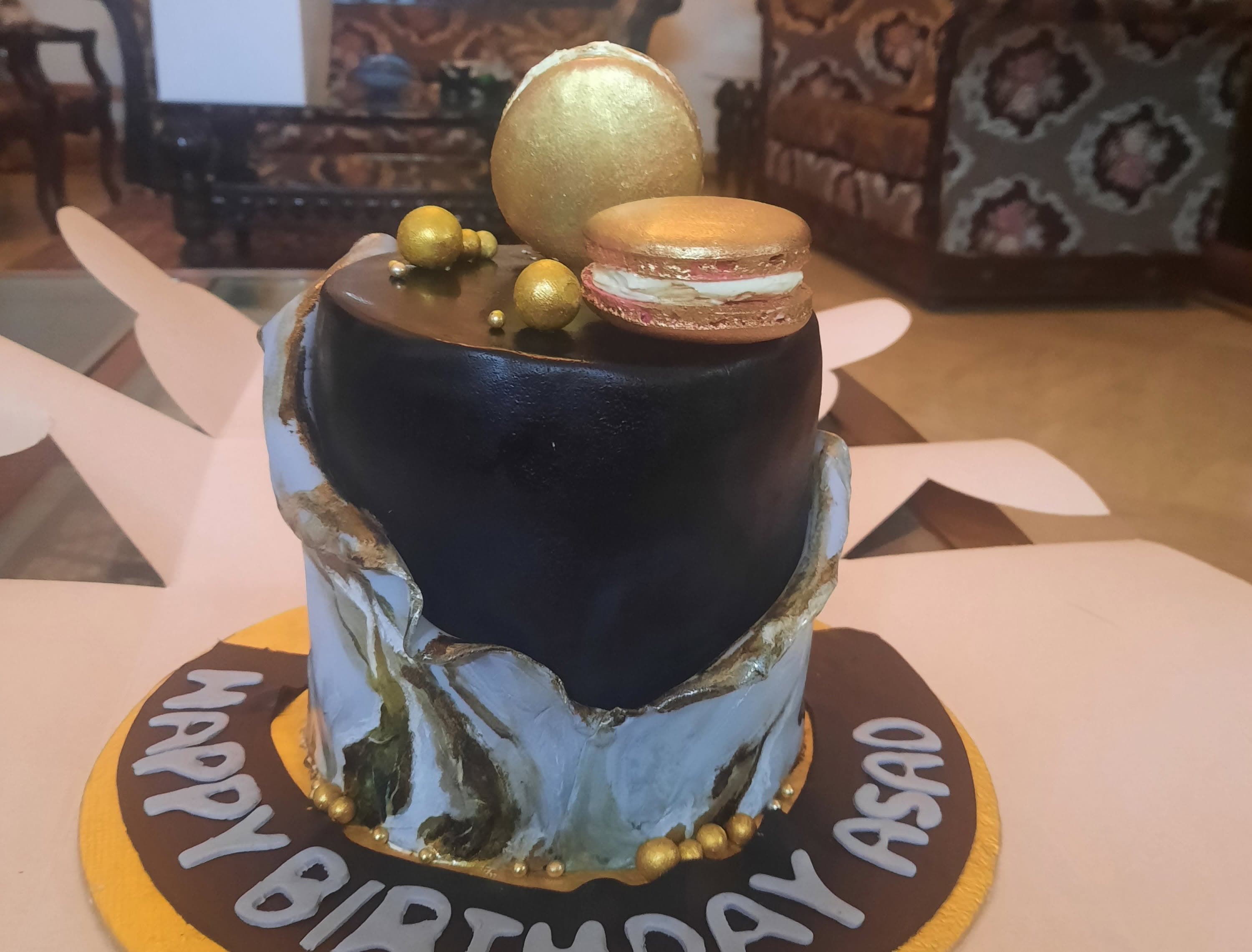 A tall cake with black and marble-style panels, gold accents, and round decorative toppers.