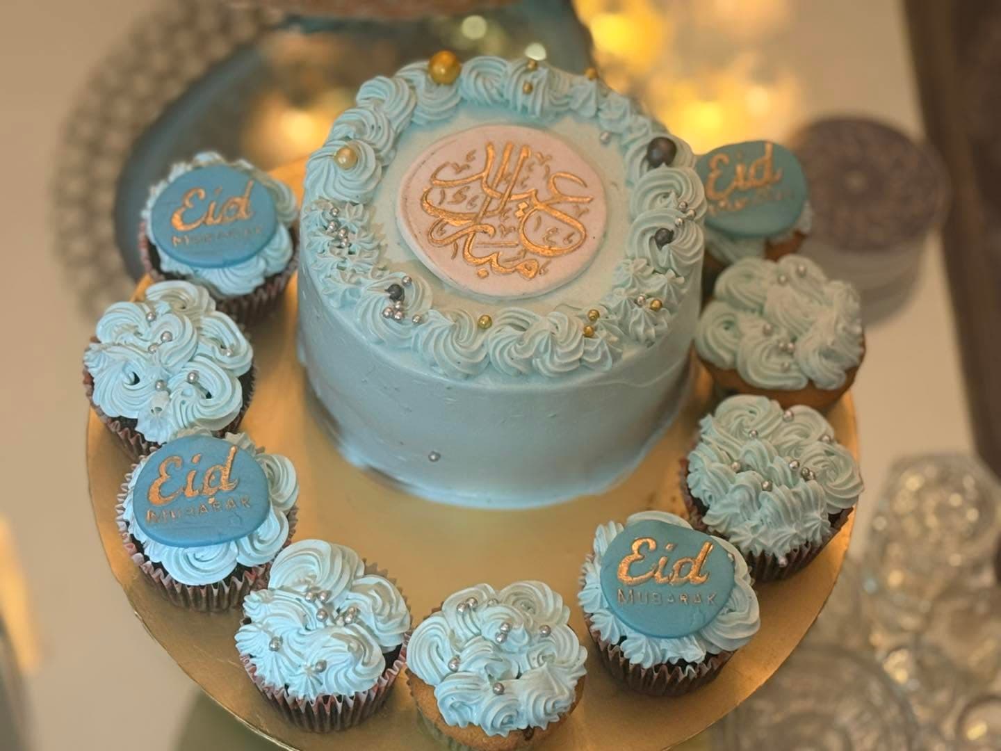 A pale blue cake surrounded by matching decorated cupcakes and round message toppers.