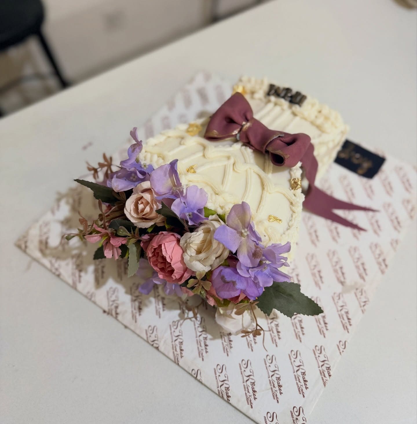 SK Bakes floral cake with soft purple flowers, cream icing and a mauve bow