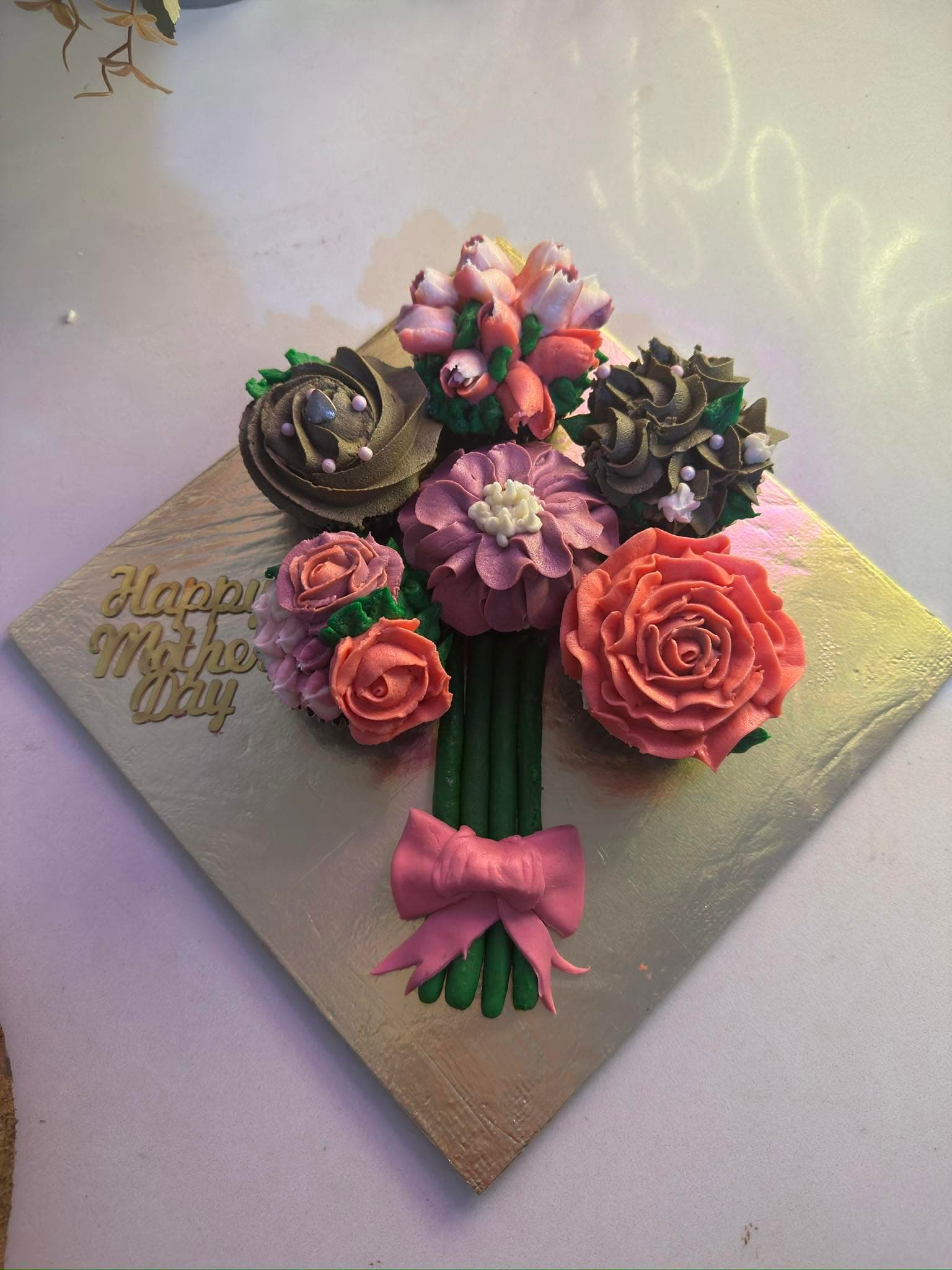 A bouquet-style cupcake arrangement with pink, purple, and cream floral decorations and a pink bow.