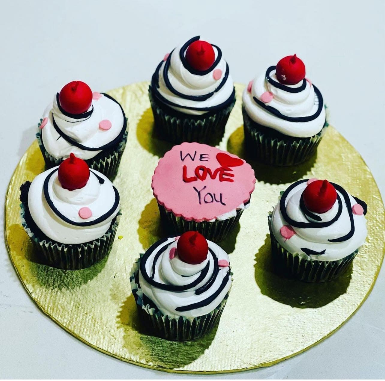 Cupcakes with white swirls, dark outlines, red toppers, and a pink message centerpiece.