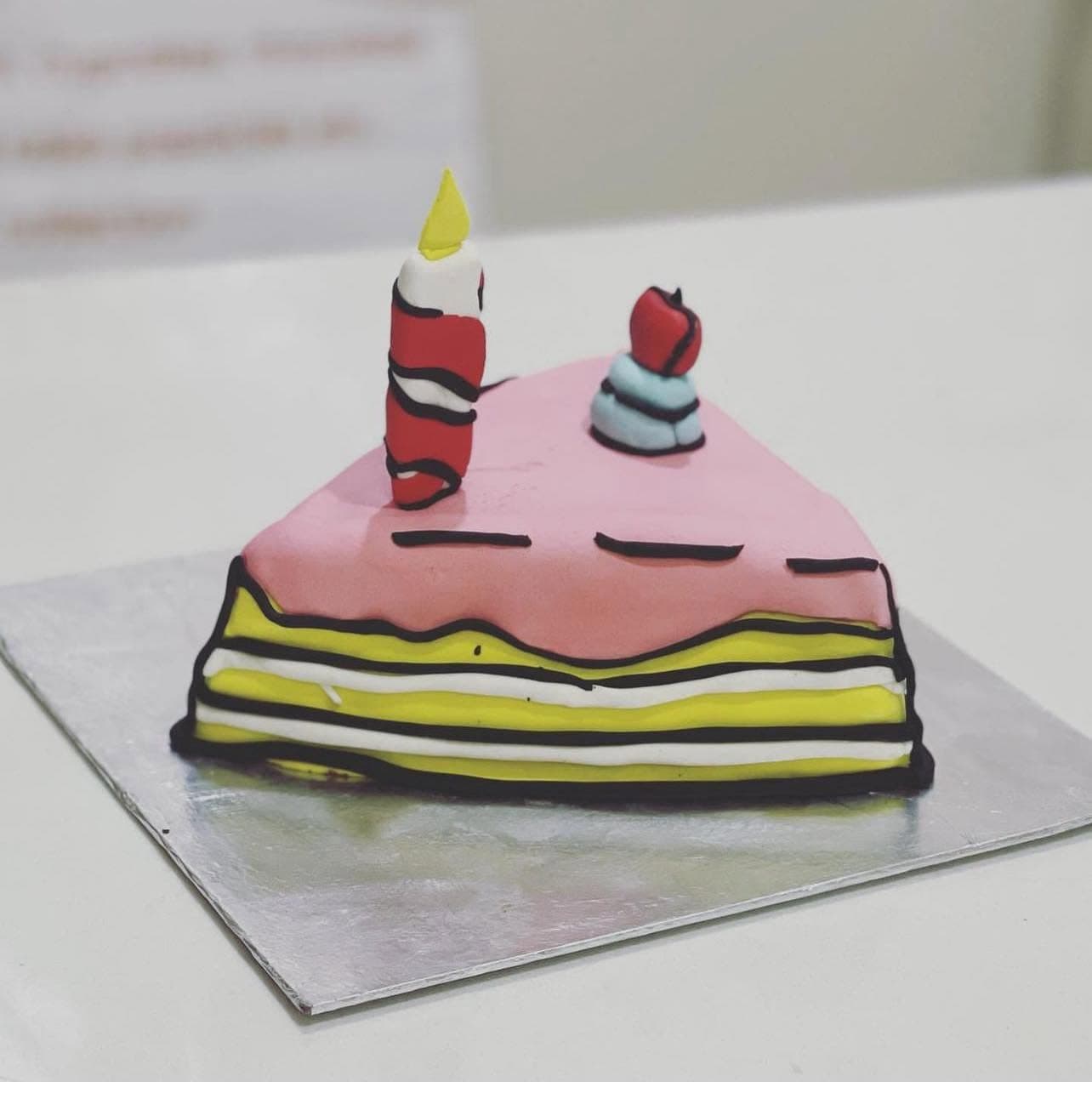 A slice-shaped cake with pink and yellow layers, dark outlines, and candle decorations.