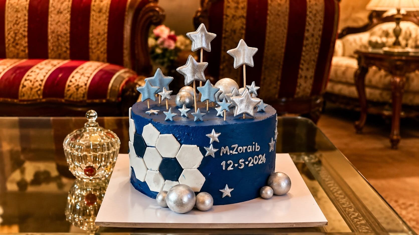 A blue football-themed cake with white ball shapes and blue and silver stars. Alternate view.